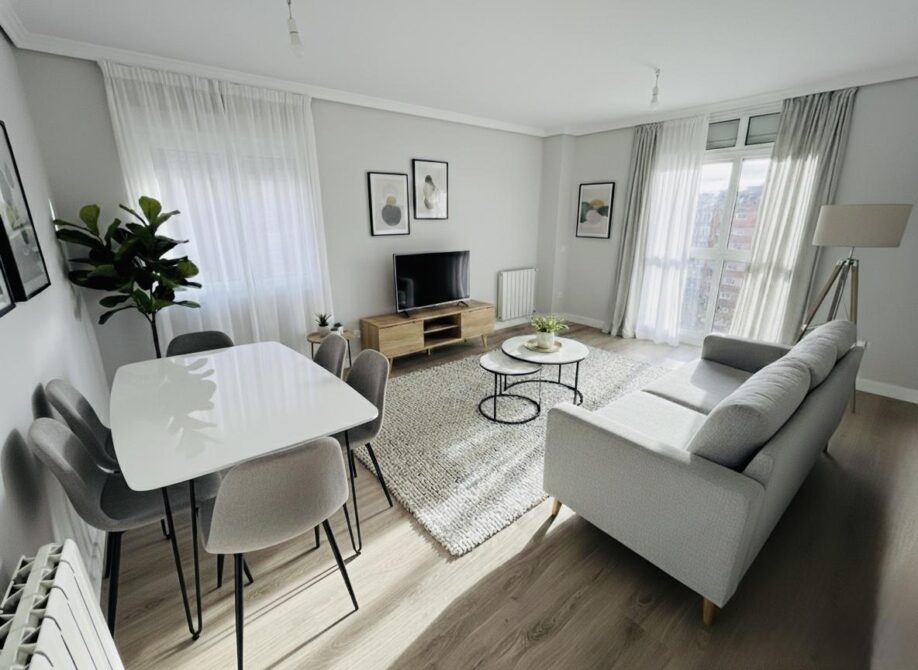 Salón luminoso de vivienda reformada en Las Tablas, Madrid, con ventanas de mirador, suelo de tarima y acabados modernos en tonos neutros