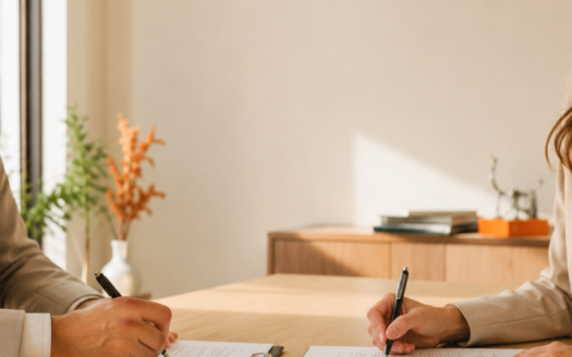Firma de escritura de compraventa en notaría con documentos y llave de vivienda sobre mesa, asesor inmobiliario de amâbit revisando la operación
