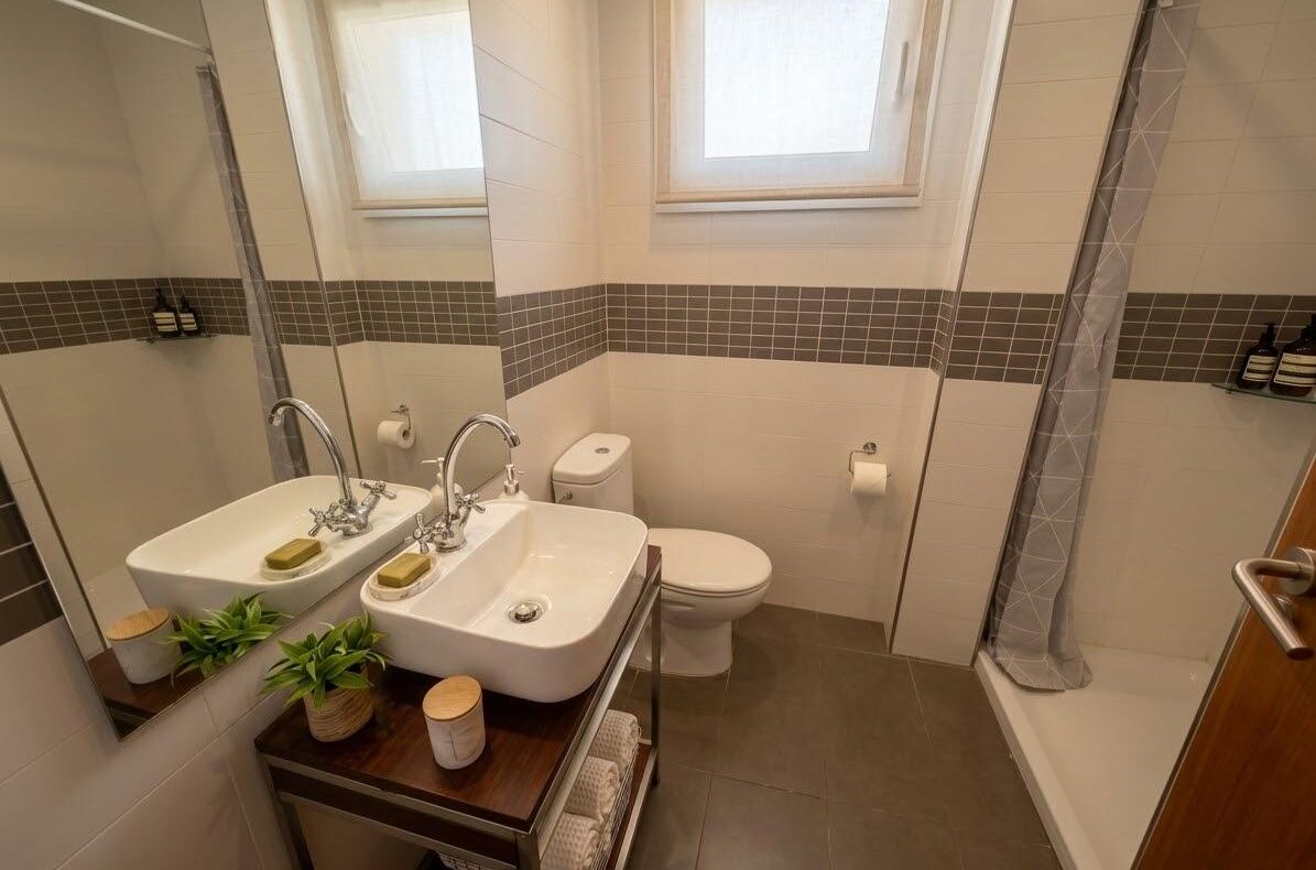 Modern bathroom with a double-sink vanity, large mirror, toilet, and shower with gray tiled accent wall.