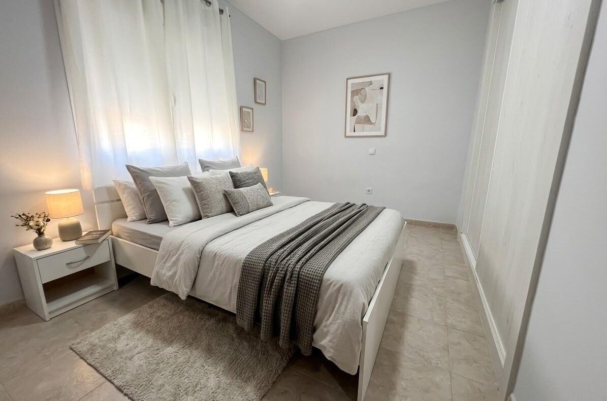 Minimalist white bedroom with a king bed, grey bedding, and soft lamps on nightstands
