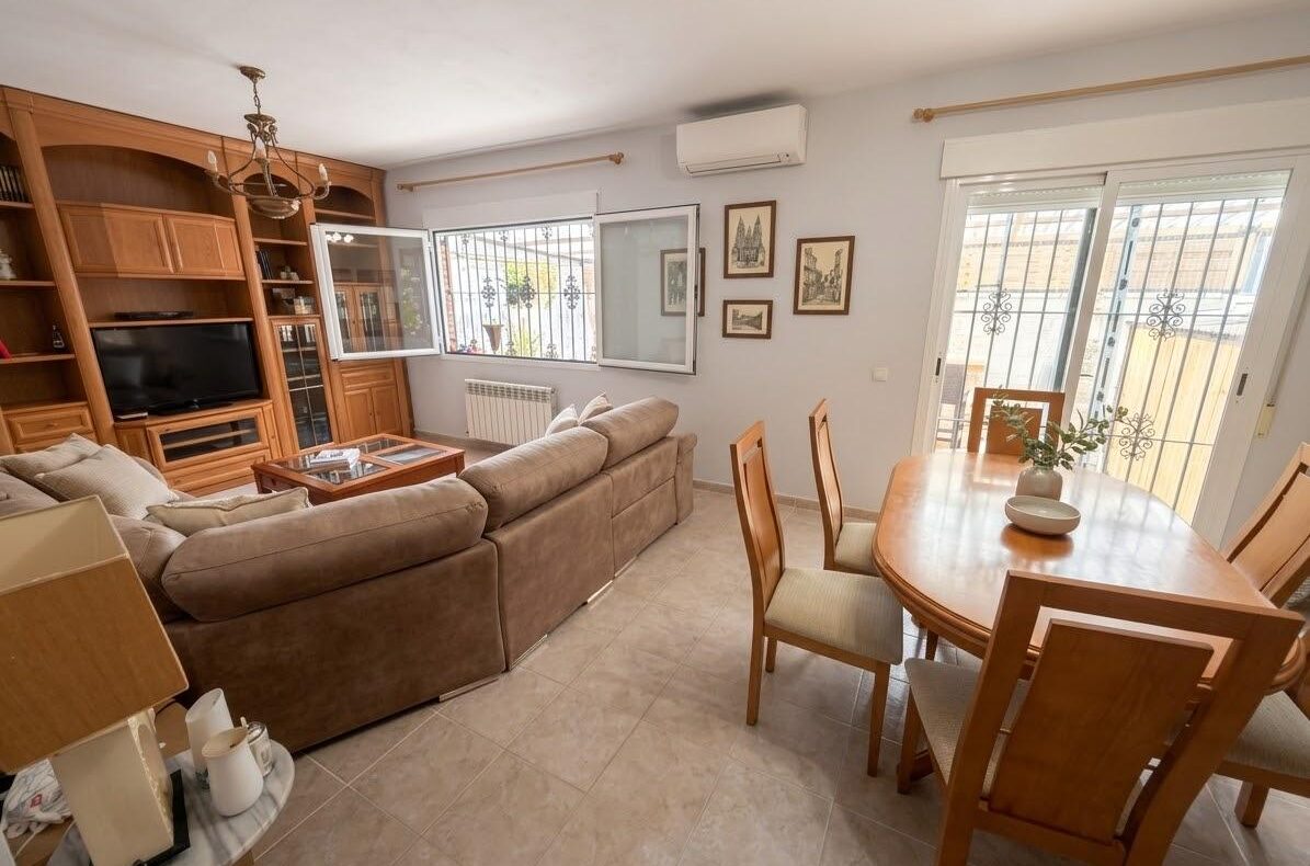 Living room with a large brown sectional sofa facing a wooden entertainment unit and TV, beige walls, and tiled floor.