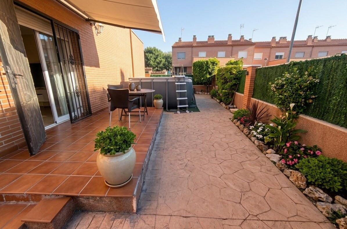 Patio area with terracotta tiles, a round table and chairs under an awning, potted plant on steps, and a fenced garden path leading to an above-ground pool.