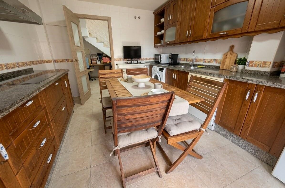 Wooden-kabinet kitchen with a rectangular dining table set for four and cushioned chairs in the center.