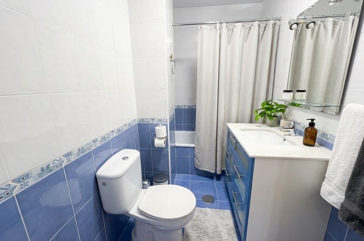 A compact blue-and-white bathroom with a toilet, vanity, and a shower curtain visible in the corner.