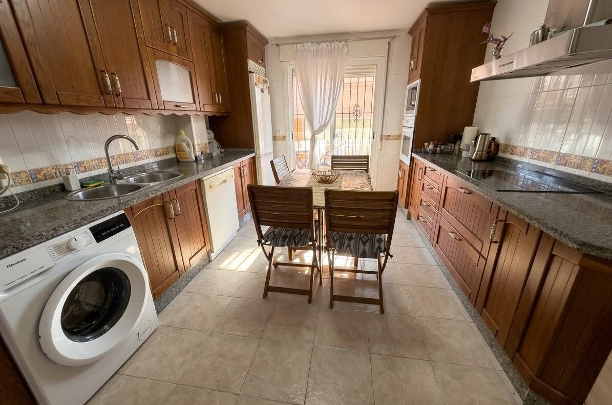 Cozy kitchen with dark wood cabinets, granite countertops, and a central wooden dining table with four chairs.